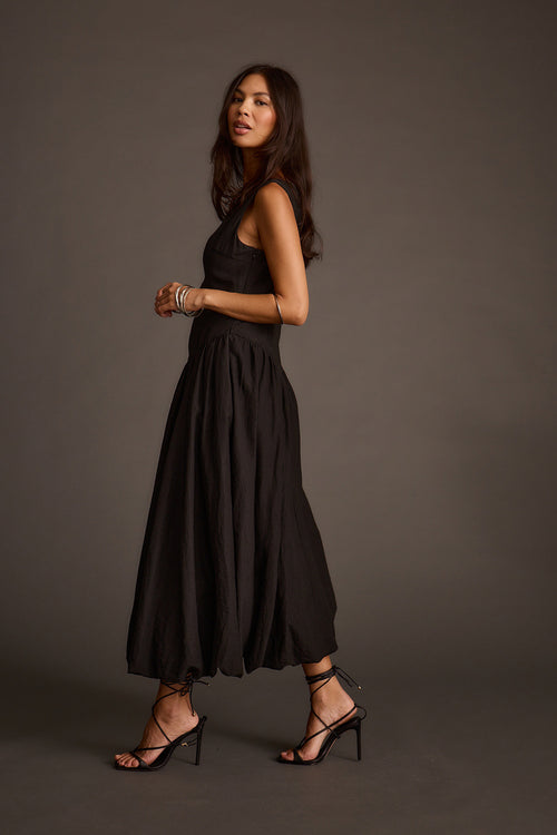 Woman walking in a sleeveless black midi dress with strappy high-heeled sandals