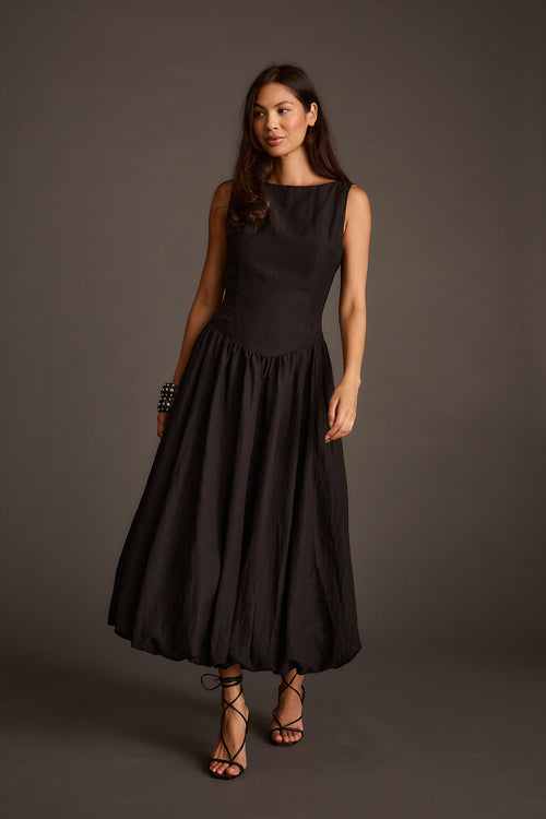 Woman modeling a sleeveless black midi dress with a bubble hem and lace-up heeled sandals