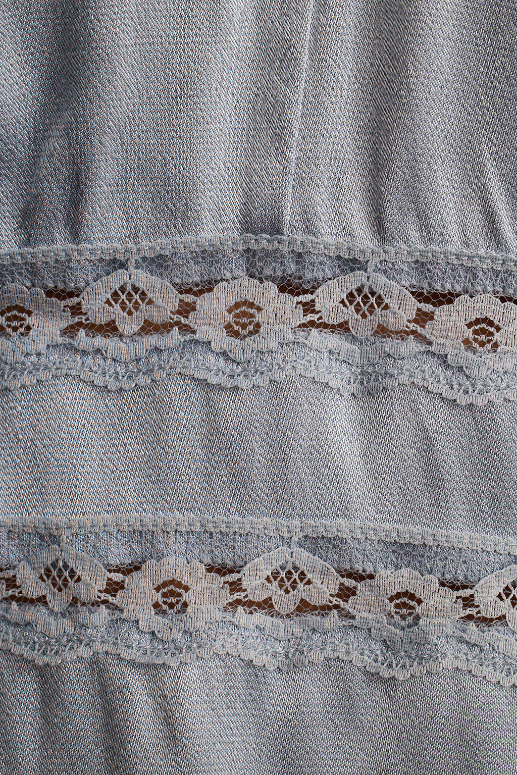 Close-up of chambray denim fabric with a scalloped lace trim insert.