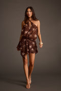 Brown floral chiffon halter mini dress with crisscross straps, a drop waist, and gold bangle bracelets.