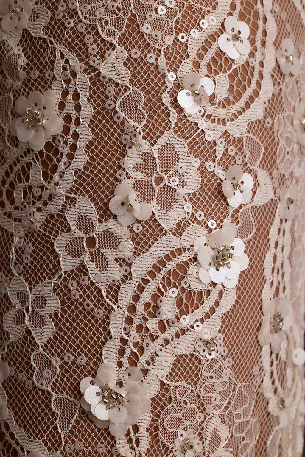 Close-up of ivory sequin lace fabric with a floral paisley pattern.