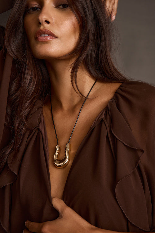 Woman wearing gold bolo necklace with horseshoe pendant and ruffled blouse