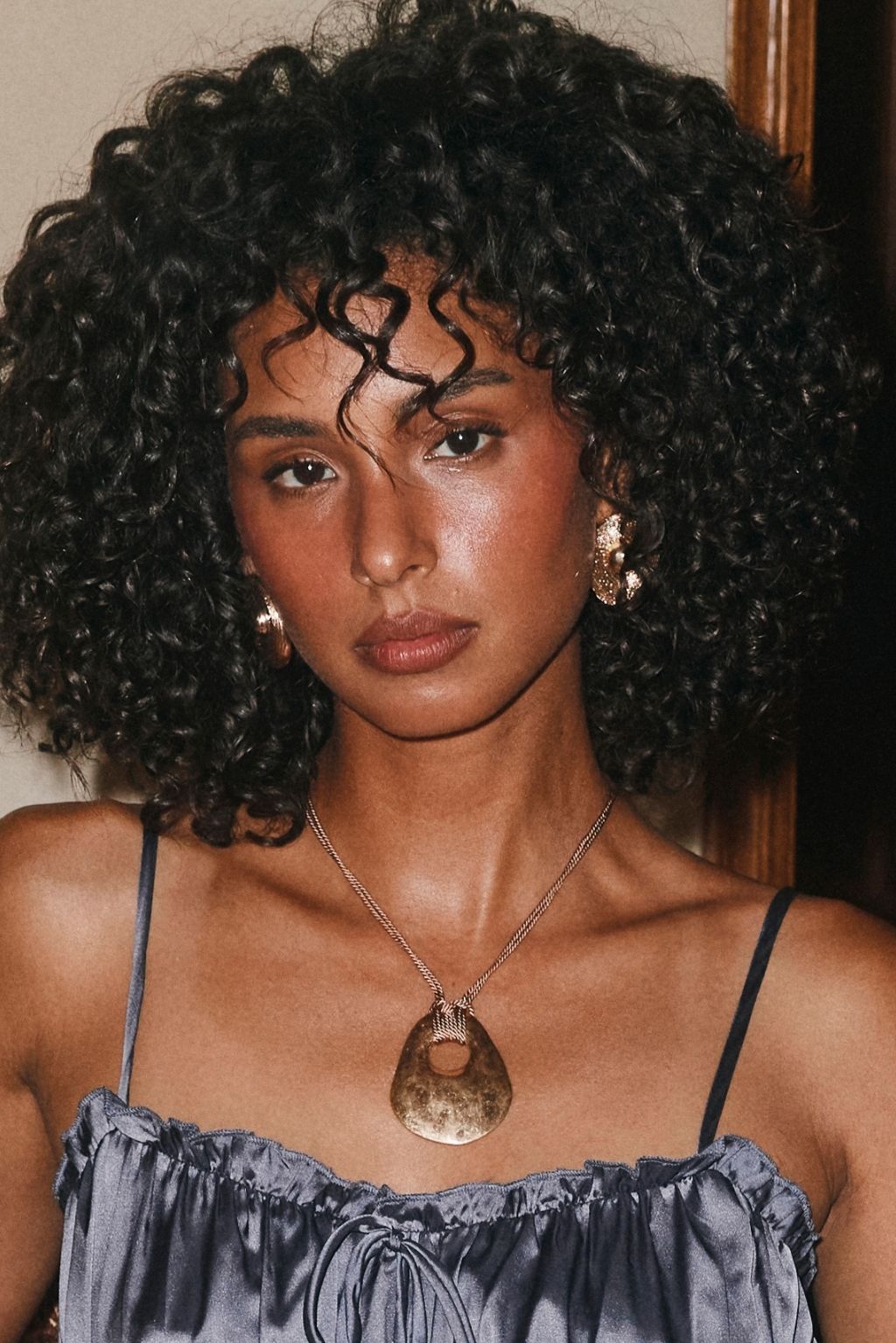 Close-up of a woman wearing a gold pendant necklace with a teardrop-shaped stone and gold hoop earrings