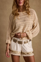 Model wearing the 12th Tribe Marela Cream Crochet Sweater, featuring open-knit stretch material, styled with the Nayeli Gold Embellished Shorts and Lioran Gold and Silver Statement Belt.