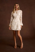 Ivory floral mini dress with sheer long sleeves, styled with gold heels and jewelry.