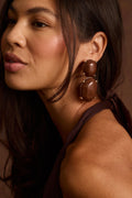 Brown resin double-drop earrings with gold prong settings, styled on the ear.