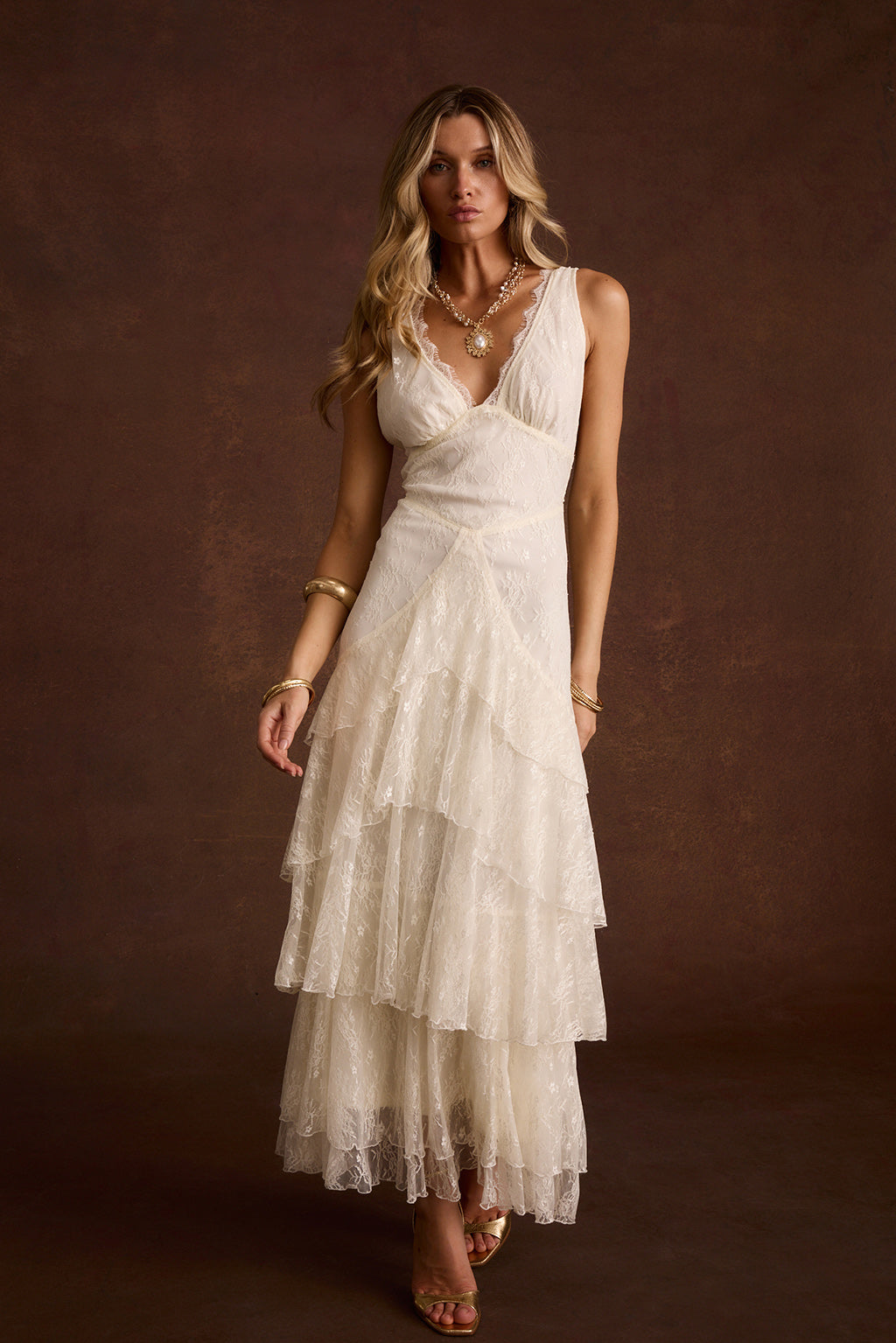 Cream lace maxi dress with V-neck and tiered ruffle skirt, styled with gold sandals.