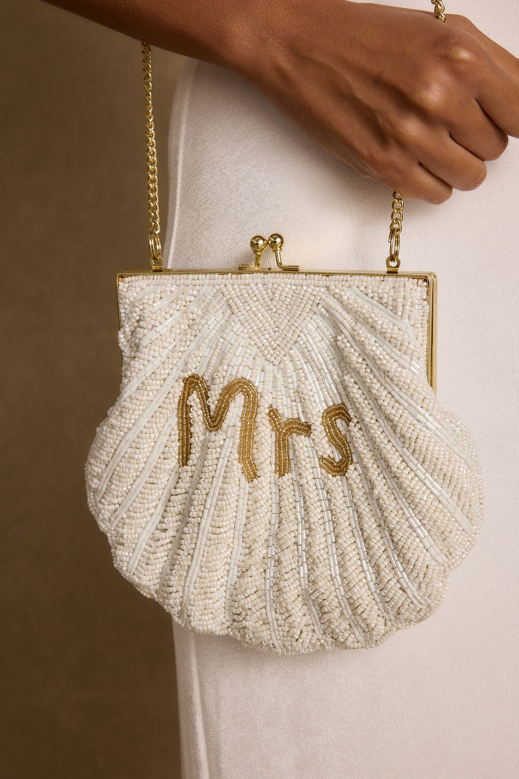 Model carrying the 12th Tribe MRS Beaded Shell Bag, a white beaded clutch featuring shell lettering and a structured silhouette, styled for bridal events, bachelorette parties, and honeymoon celebrations.