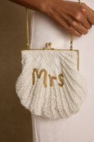 Model carrying the 12th Tribe MRS Beaded Shell Bag, a white beaded clutch featuring shell lettering and a structured silhouette, styled for bridal events, bachelorette parties, and honeymoon celebrations.