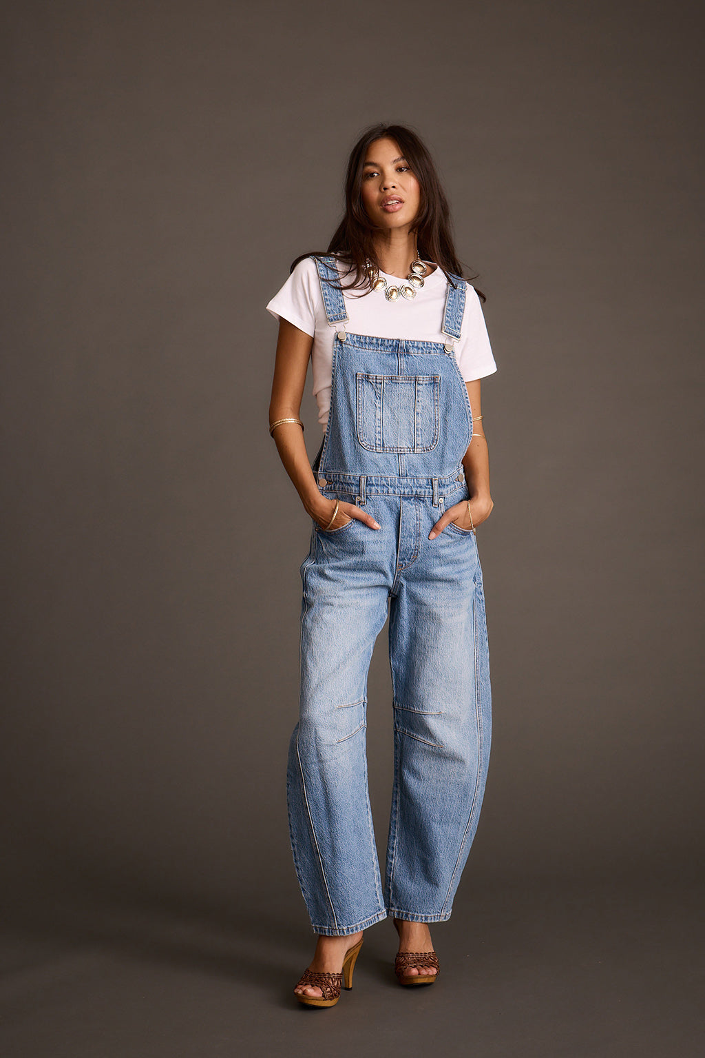 Woman modeling light-wash blue denim barrel-leg overalls, front view