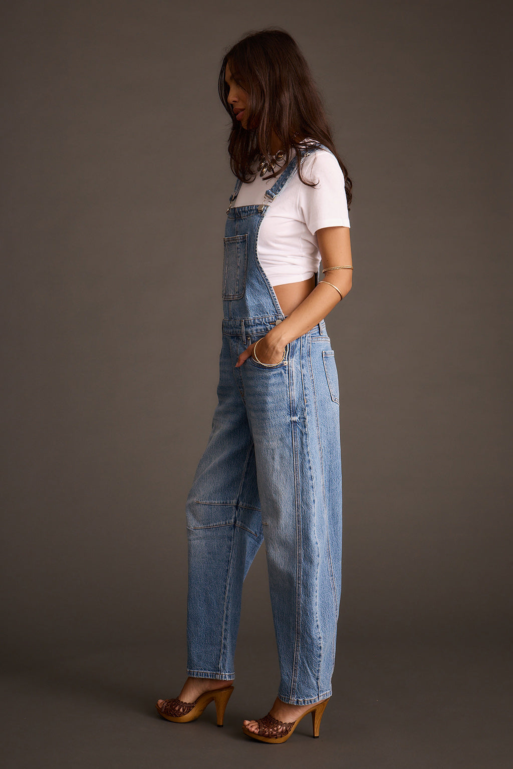 Woman wearing light-wash blue denim barrel-leg overalls, side profile view