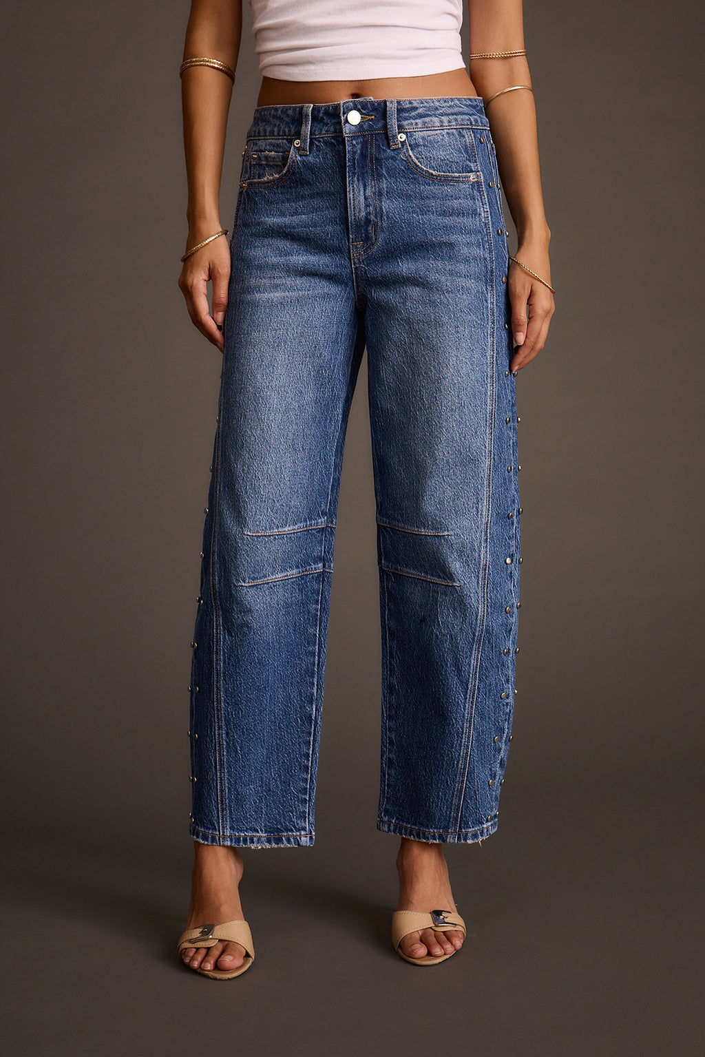 Women's studded barrel jeans styled with a white crop top and beige slide sandals, front view