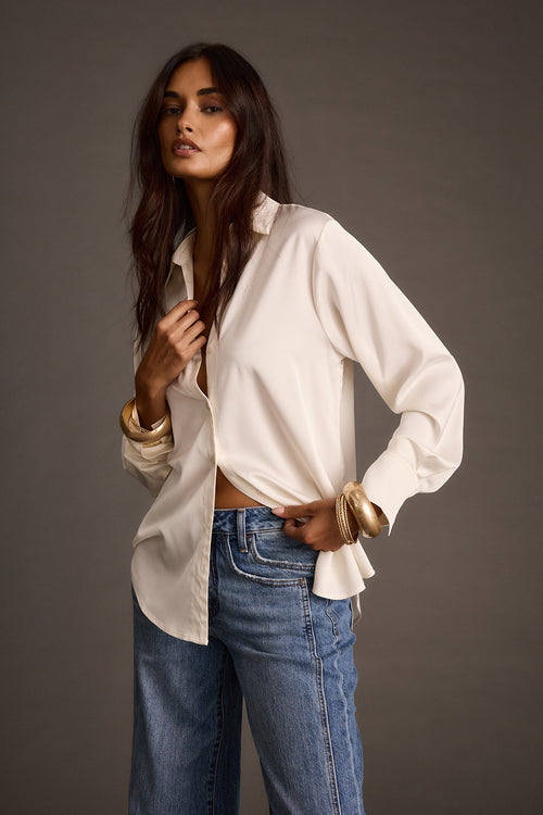 Woman modeling ivory satin button-down shirt with blue jeans and gold bracelets