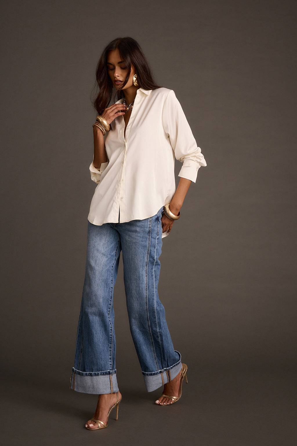 Woman modeling ivory satin button-down shirt with wide-leg blue jeans and gold jewelry