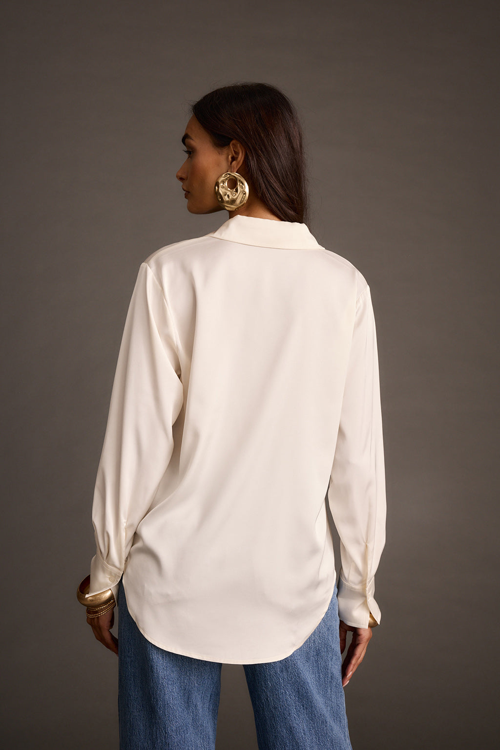Woman wearing ivory satin button-down shirt with blue jeans, back view