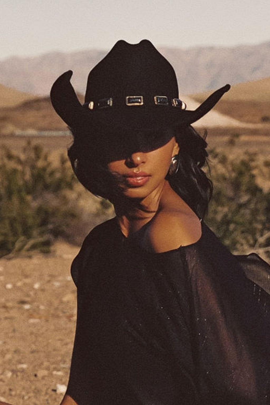 McGraw black onyx cowboy hat with ornate buckle band detail worn by woman in desert landscape with mountains in background.