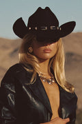 Close-up of black onyx cowboy hat with silver concho hatband worn with a leather jacket in a desert landscape.