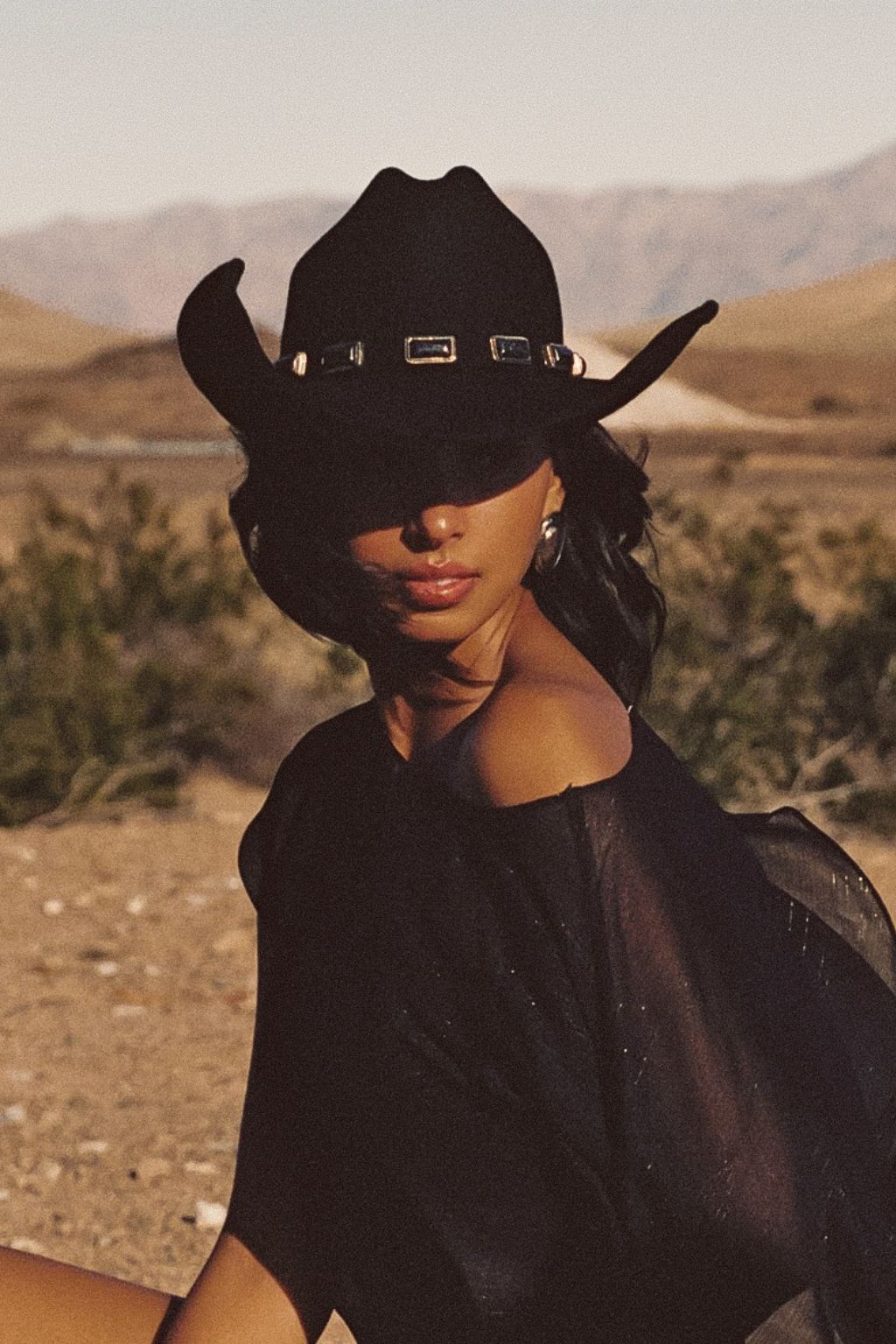 Black onyx western cowboy hat with upturned brim and buckle band against a desert mountain backdrop.