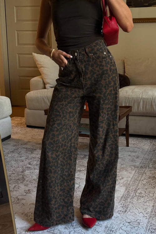 Woman wearing high-waisted wide leg leopard print jeans with a black tank top, red pointed-toe heels, and a red shoulder bag in a living room