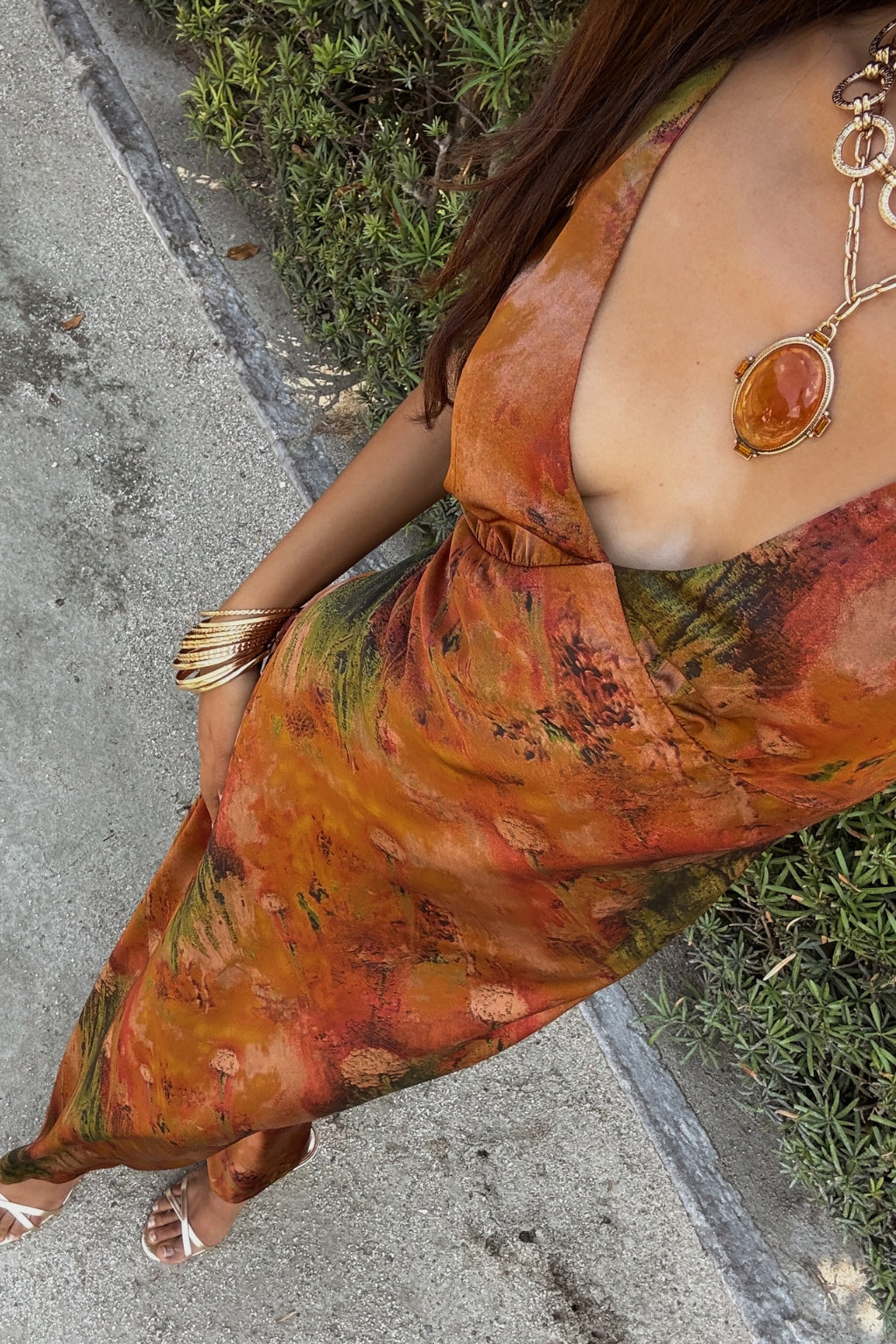 Overhead angle on the Mirabella rust printed satin maxi dress, gold pendant and white sandals.