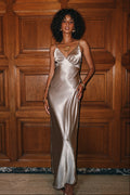 Taupe satin V-neck slip maxi dress with a wrap bodice, round gold pendant necklace, and gold bangle bracelets.