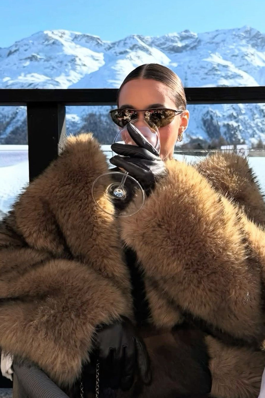 Person wearing a fur coat and sunglasses with a snowy mountain background