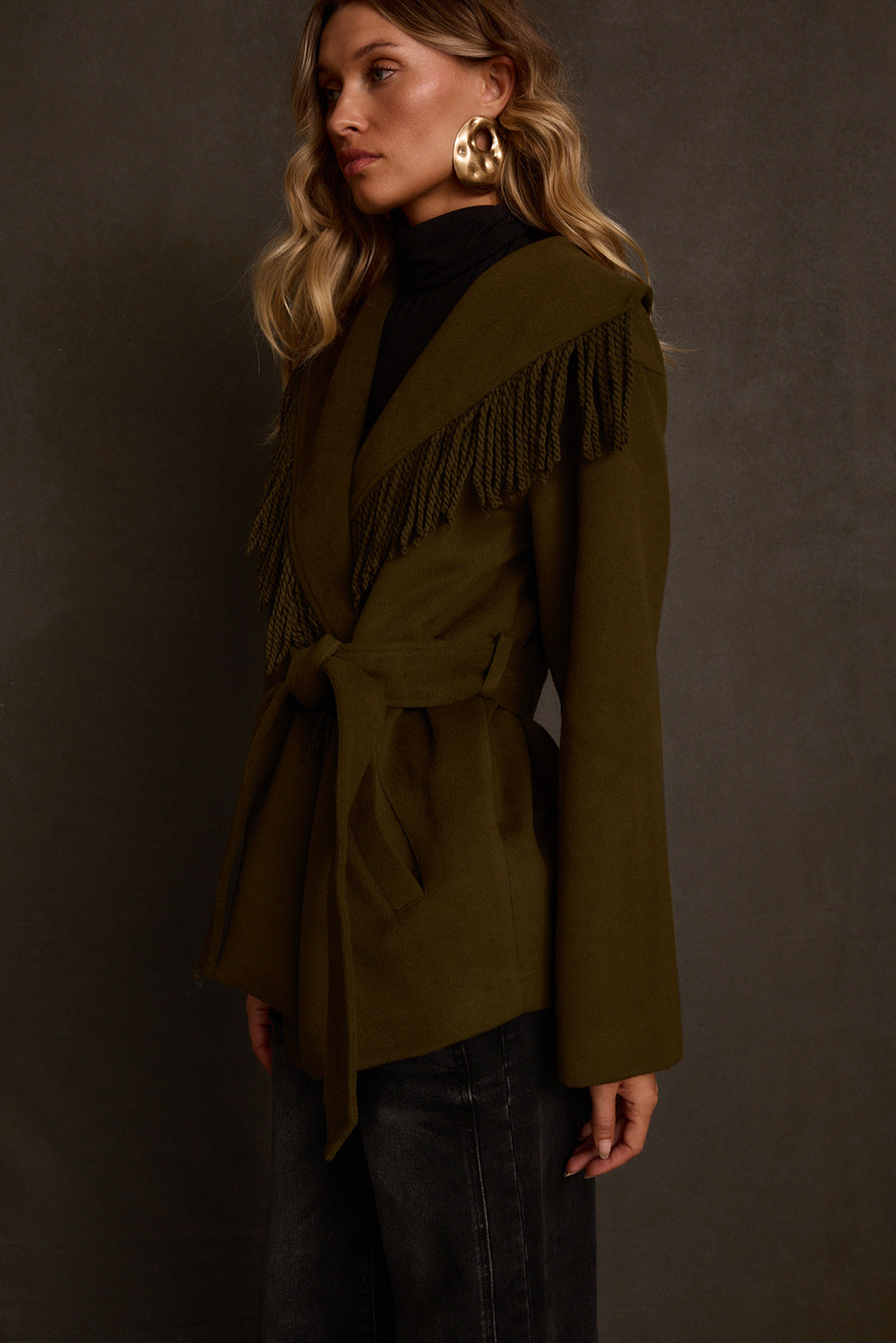 Fall coat side view with rope fringe trim along shawl collar and belted waist
