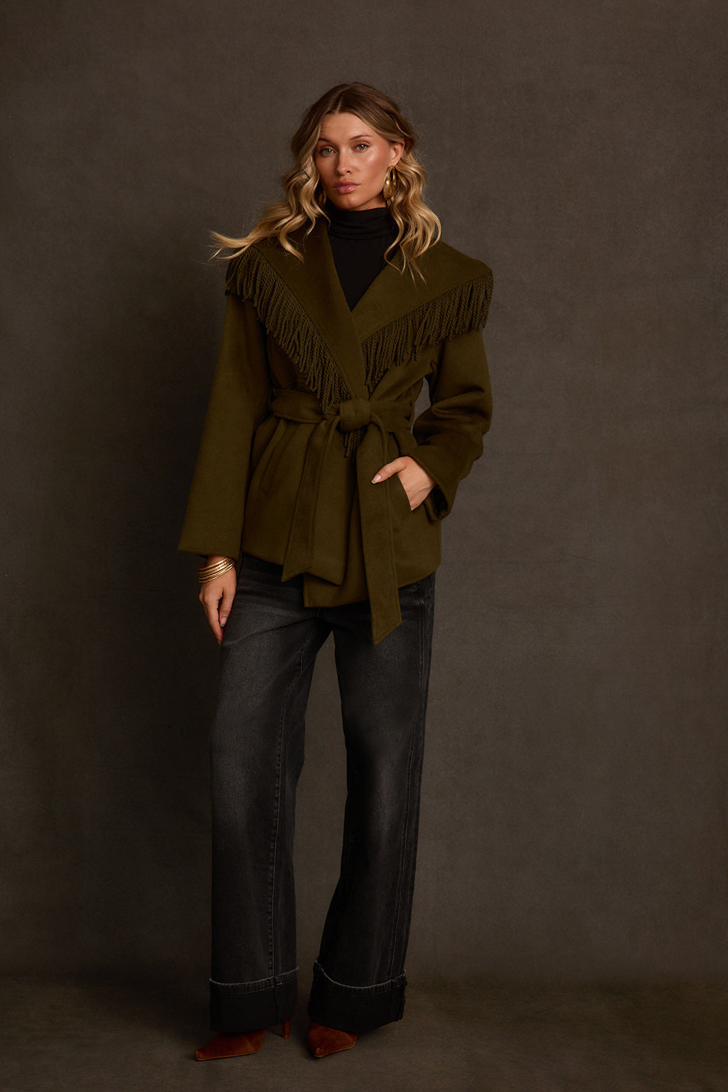 Belted coat three-quarter angle showing olive wool fabric and twisted rope fringe trim