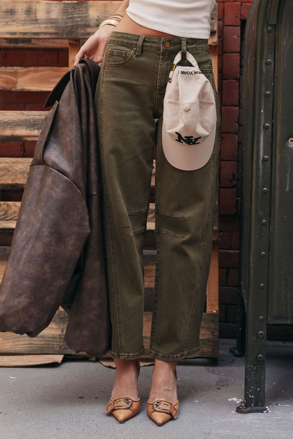 Olive green barrel-leg jeans styled with leopard-print heels and a white baseball cap