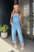 Woman wearing light wash barrel-leg denim overalls with cuffed hems, a white tank, beige knit headband, and pointed beige heels.