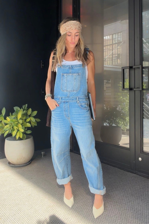 Woman wearing light wash barrel-leg denim overalls with cuffed hems, a white tank, beige knit headband, and pointed beige heels.