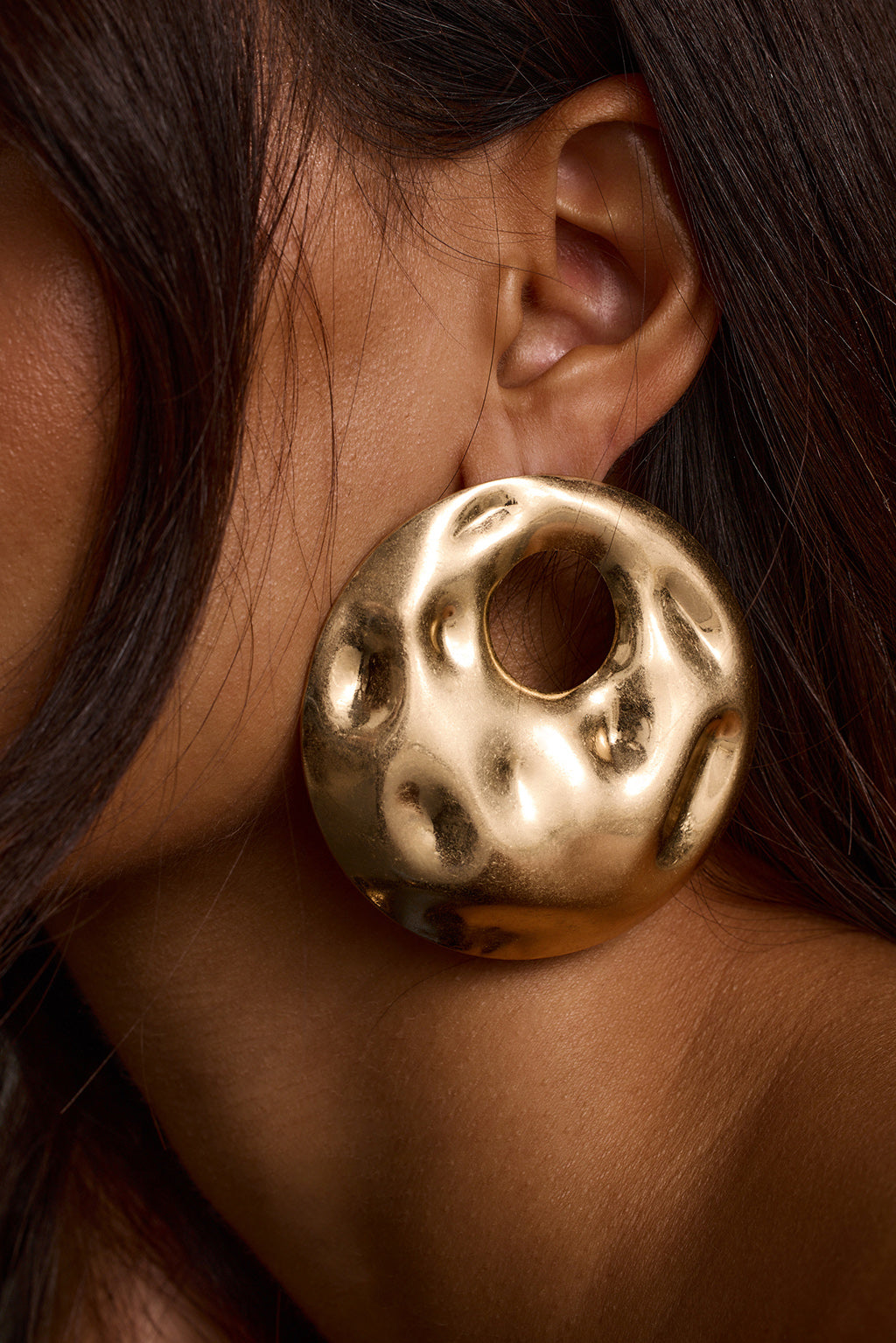 Close-up of gold statement earrings with a textured donut-shaped design