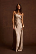 Taupe strapless satin column dress with a gold pendant necklace and layered gold bangle bracelets.