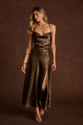Olive satin cowl neck slip dress with thin straps, a thigh-high slit, and gold bangle bracelets.
