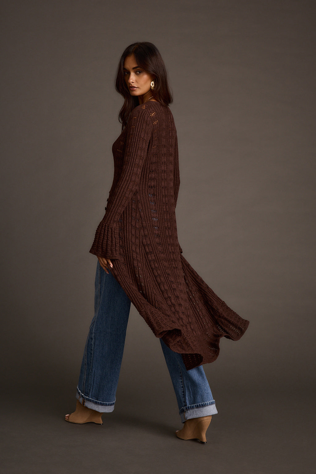Women's espresso knit longline cardigan styled with jeans, side profile walking view
