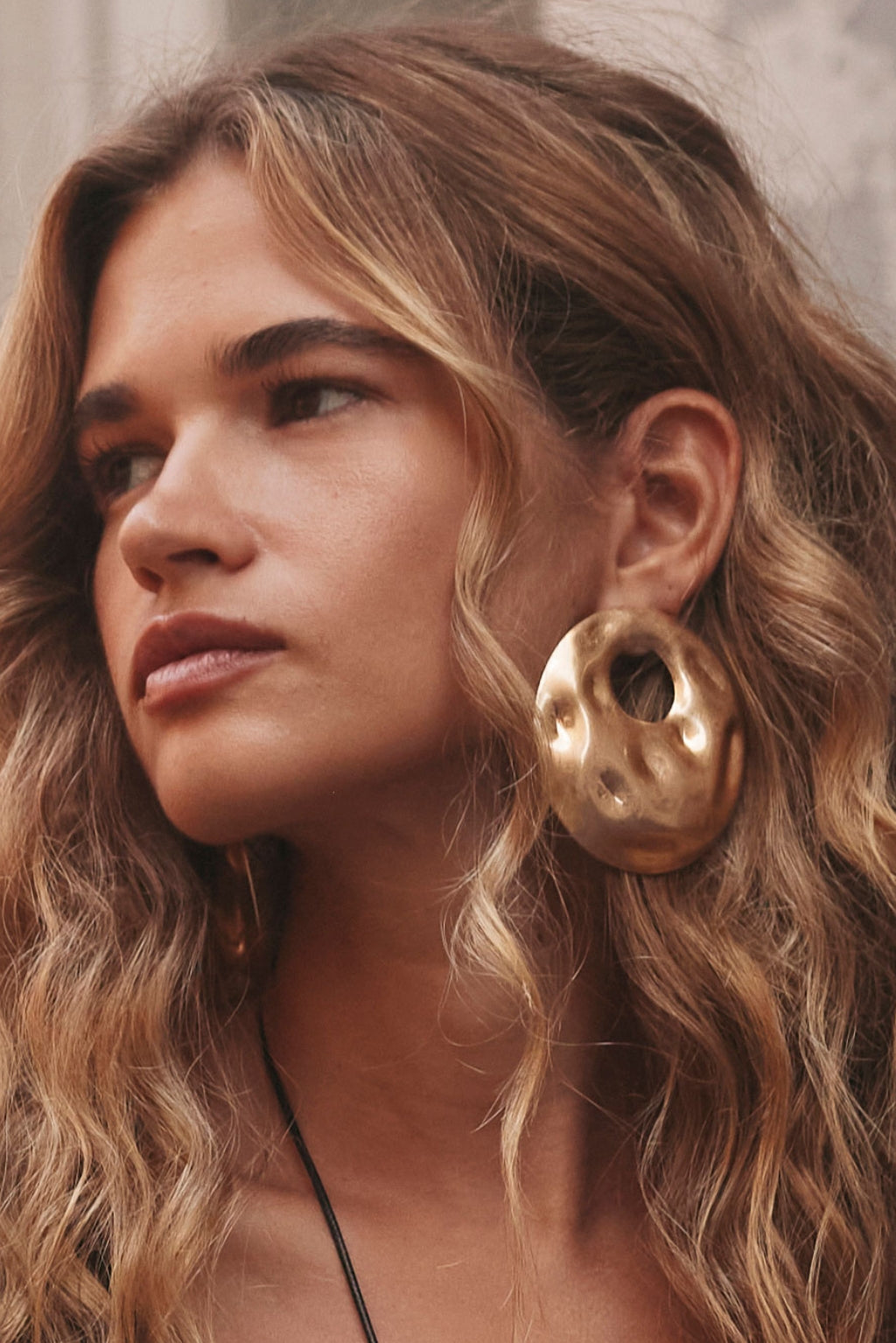 Woman with wavy hair wearing a large textured gold hoop earring