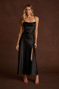 Black satin cowl neck slip dress with thin straps, a side slit, and gold bangle bracelets.