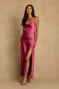 Model wearing the 12th Tribe Natalia Fuchsia Satin Maxi Dress in a bold and sexy pink satin. Featuring a flowing maxi silhouette and flattering cowl neckline. Style with strappy heels for bachelorette parties, vacation dinners, and wedding celebrations.