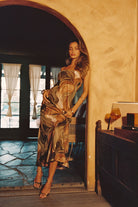 Model wearing the 12th Tribe Natalia Olive and Rust Abstract Strapless Maxi Dress, a best seller in a new olive and rust colorway with a strapless neckline and flowing maxi-length silhouette.