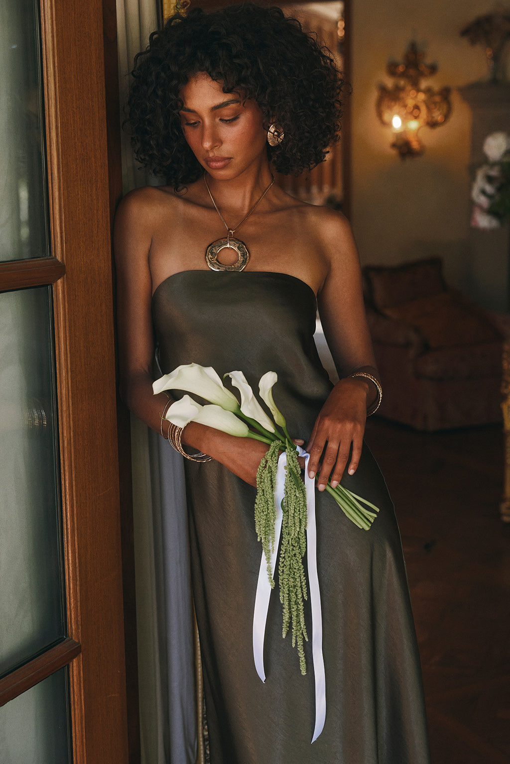 Close-up of an olive satin strapless dress bodice with a statement gold pendant necklace.