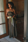 Olive satin strapless maxi dress with an oversized gold pendant necklace and layered gold bracelets.