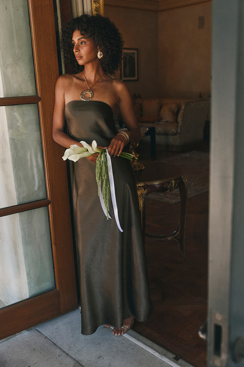Olive satin strapless maxi dress with an oversized gold pendant necklace and layered gold bracelets.