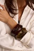 Close-up of a chunky resin cuff bracelet in amber and olive tones over a cream satin sleeve