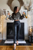 Woman in black sequin top and leather pants standing in a room with decorative lights and a fireplace.