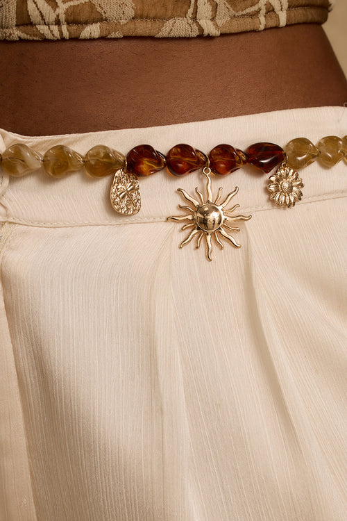 Close-up of gold sun charm belt with amber and clear stones over cream skirt.