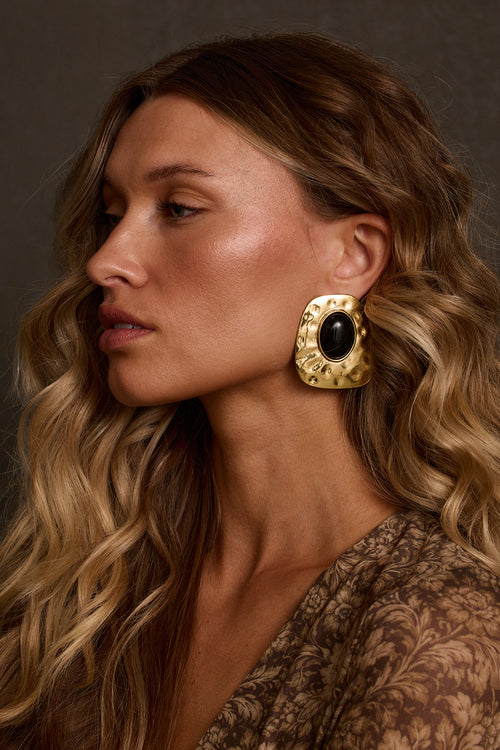 Gold earrings with hammered frame and oval black stone center, close-up profile on model