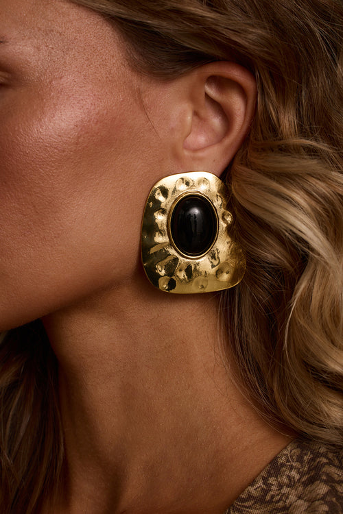Statement earrings in gold with black cabochon stone, worn with mesh floral top and turtleneck