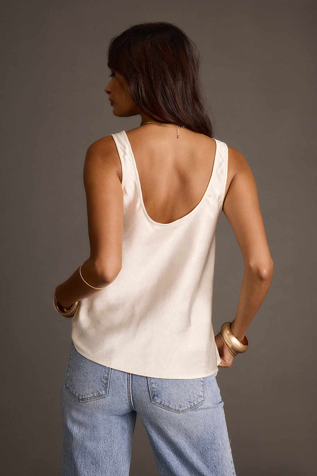 Women's ivory satin tank top styled with light-wash jeans, back view