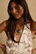 Layered gold pendant necklace with a marbled grey stone centerpiece worn over a floral halter top.