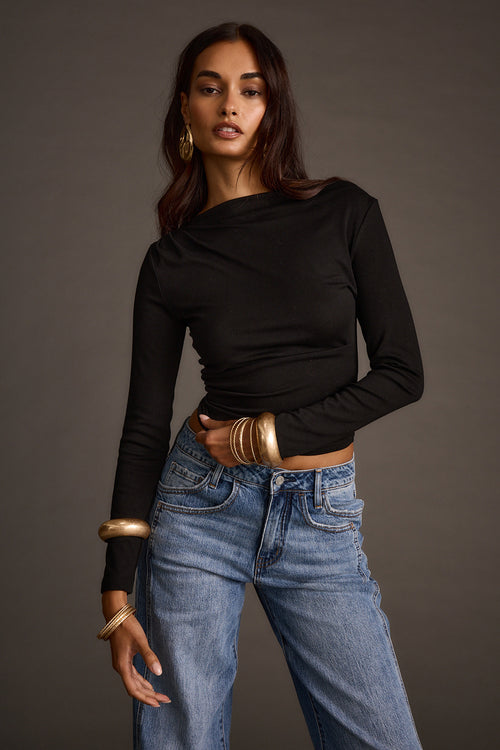 Woman wearing a black off-the-shoulder top with wide-leg jeans and stacked gold bangles
